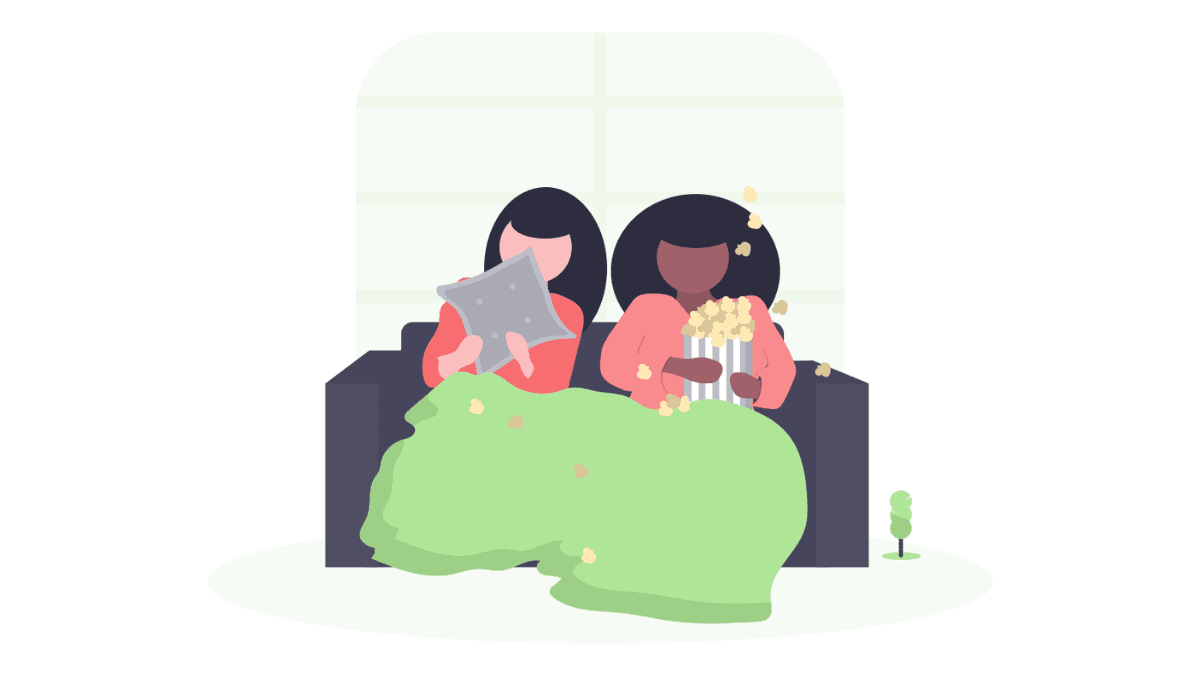 Two individuals sitting in a cozy couch with a blanket while eating popcorn.